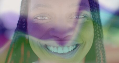 Smiling woman with braided hair showing colorful light patterns on face in studio, abstract art