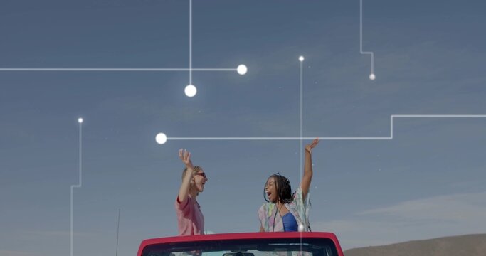 Driving red convertible, two women raising arms on rural road under blue sky, network overlay