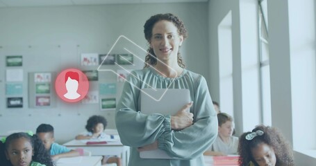 Holding tablet binder, teacher guiding students writing on papers in sunlit classroom by windows