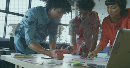 Coworkers collaborating in open office, pointing at pie charts and bar graphs with sticky notes