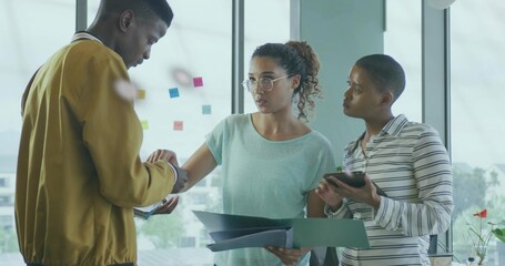 Coworkers in mustard jacket collaborating at office window with ring binder tablet and sticky notes