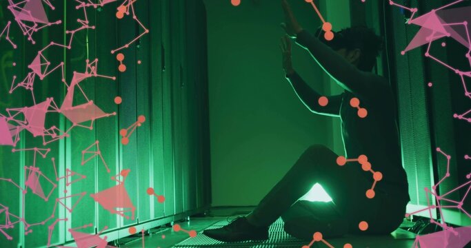 Kneeling technician in dark outfit touching server rack in datacenter green lighting, pink overlay