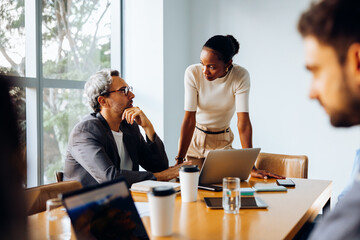Two colleagues discussing work in an office with laptops and documents