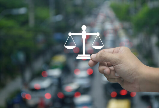 Hand holding law flat icon in fingers over blur of rush hour with cars and road in city, Business legal service concept