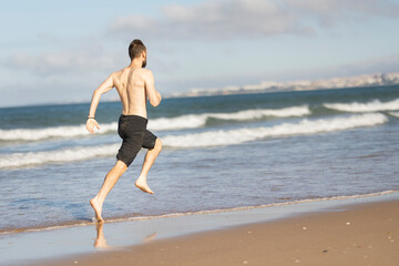 Young man running barefoot on sandy beach