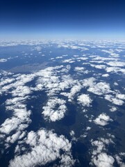 High-altitude aerial view from an airplane window, looking down on scattered white clouds over a coastal city and the sea under a clear, deep blue sky, illustrating themes of travel and perspective.