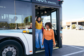 Two young women friends getting off a modern electric city bus, traveling and using public transportation for urban commuting
