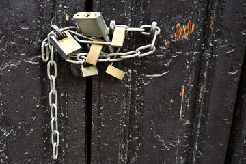 Several padlocks and a metal chain securing an old wooden door, symbolising protection and...