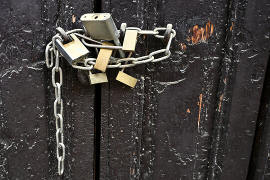 Several padlocks and a metal chain securing an old wooden door, symbolising protection and restriction.