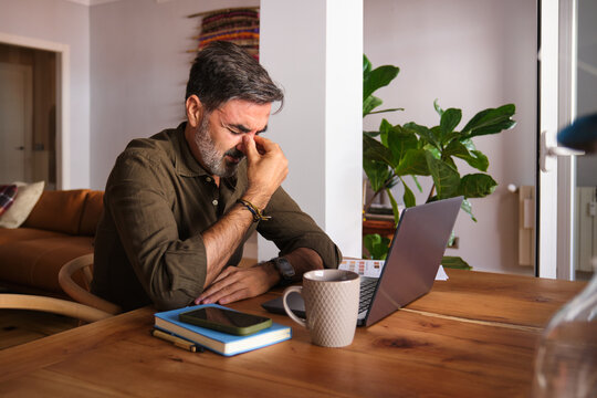 Overworked man with headache working at laptop in home office
