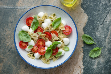 Plate of caprese pasta salad with farfalle, horizontal shot on a beige and grey granite background, above view