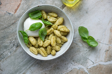 Bowl of italian gnocchi with mozzarella ball and basil oil, horizontal shot on a grey granite background, flat lay
