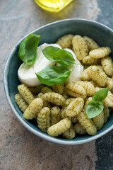 Potato gnocchi with basil oil, mozzarella and fresh basil served in a green bowl, vertical shot on a beige granite background, middle closeup