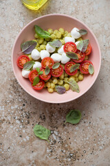 Bowl of italian mini potato gnocchi with cherry tomatoes and mozzarella balls, vertical shot on a beige granite background, above view