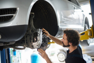 Skilled mechanic is working on a vehicle's brake system in a well-equipped garage. The scene shows the detailed process of inspecting car parts for repairs.