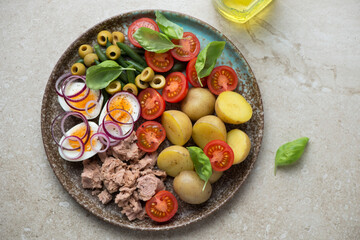 Plate with nicoise or french salad with tuna on a beige stone background, horizontal shot, flat lay