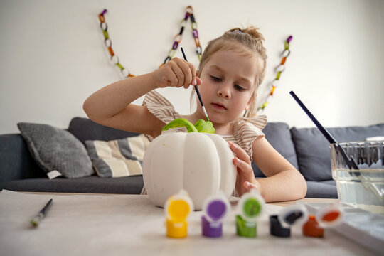 Child painting ceramic pumpkin at home as autumn craft activity