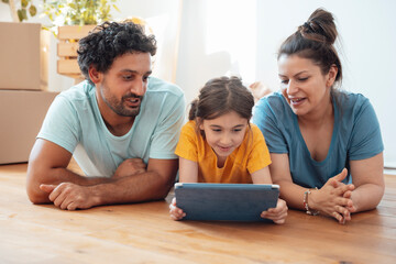 Smiling woman and man with daughter using tablet PC on floor