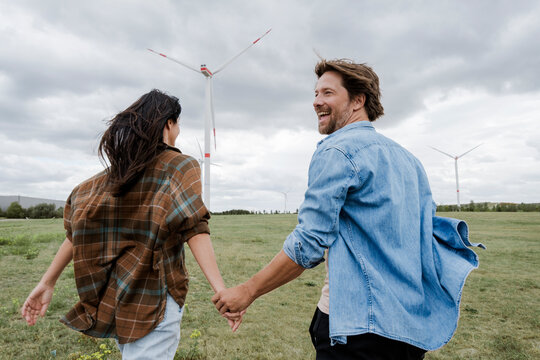 Couple holding hands by wind turbines promoting green energy