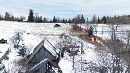 A tranquil winter panorama of Beskid Mały in southern Poland, where snowy meadows meet evergreen forests and rolling mountain hills under a serene, cloud-streaked sky.