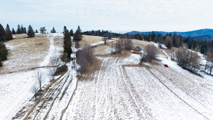 A tranquil winter panorama of Beskid Mały in southern Poland, where snowy meadows meet evergreen forests and rolling mountain hills under a serene, cloud-streaked sky.