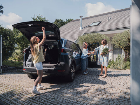 Family arriving home and happily greeting each other at car outside house