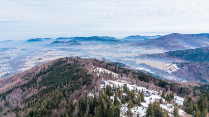 A tranquil winter panorama of Beskid Mały in southern Poland, where snowy meadows meet evergreen forests and rolling mountain hills under a serene, cloud-streaked sky.