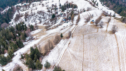 A tranquil winter panorama of Beskid Mały in southern Poland, where snowy meadows meet evergreen forests and rolling mountain hills under a serene, cloud-streaked sky.