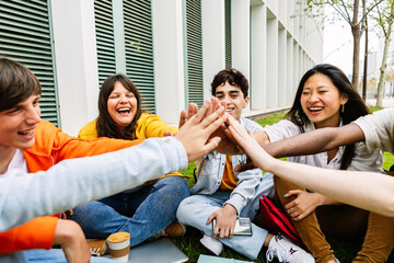 Diverse young group of students stacking hands together sitting at college campus. Support and youth community concept