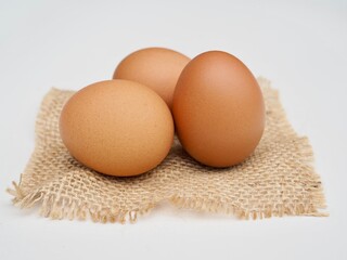 Several fresh chicken eggs are placed on a sack of cloth on a white background.