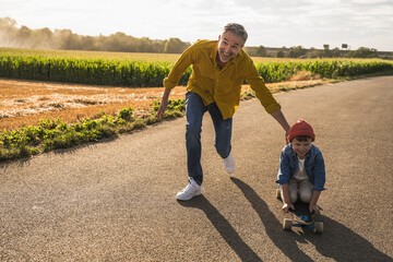 Happy man pushing grandson on skateboard on road