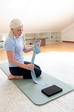 Woman preparing for exercise with resistance band on yoga mat indoors