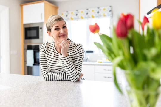 Smiling woman with hand on chin leaning on kitchen counter