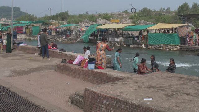 people taking a sacred dip in the narmada river at bhedaghat, with flowing waters, riverside stalls and temple visitors engaging in spiritual cleansing, jabalpur, india