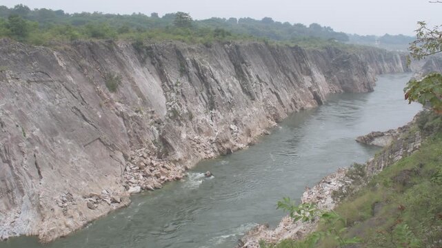 a sweeping narmada river cutting through towering marble cliffs, forming a dramatic and rugged canyon landscape