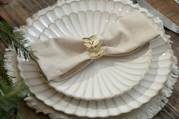 Elegant Christmas table setting with white plates, beige napkin, and decorative napkin ring 