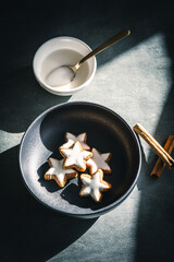 Gebackene Zimtsterne auf einem Teller und Zuckerglasur in einer Sch&uuml;ssel auf einem grauen Tisch. Draufsicht, Kekse backen.