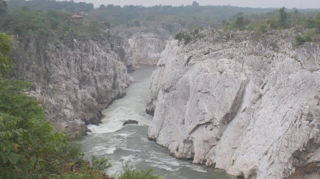 swift river currents carve their path through towering marble cliffs at bhedaghat near the dhuandhar falls, churning waters push forcefully between steep stone walls