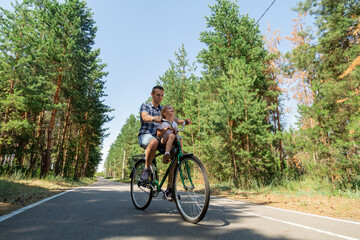 Fototapeta premium A young father carries his little daughter in a bicycle seat. Dad and child ride a bike in forest