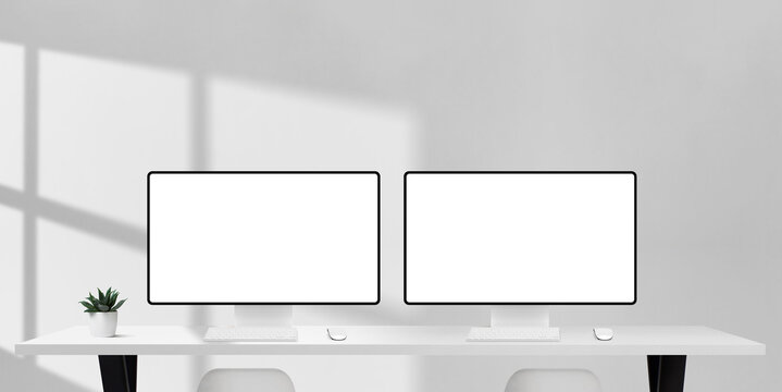Two computer monitors with blank screens on white office desk, sunlight and shadows creating bright workspace for design, teamwork, or business projects