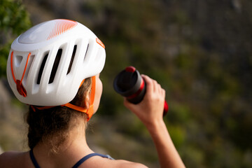 Rear view of woman athlete hydrating during break on mountain cliff with thermo cup in hand, Caucasian female taking a break with drink in nature during daytime