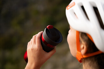 Side view of woman in climbing helmet drinking water during training break outdoors, sporty female maintaining hydration during workout in nature during daytime, close-up