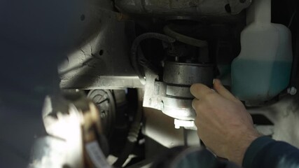 The master unscrews the bolt behind the wheel of a car with a hand tool to replace the fuel filter. home self-repair of the car. evening atmosphere, professional light