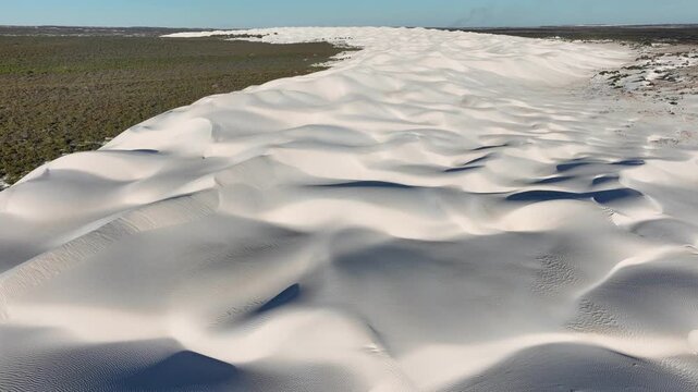 Aerial view of undulating white sand dunes contrasting with the adjacent dark green bushland, creating a striking natural landscape, Perth, Western Australia, Australia.