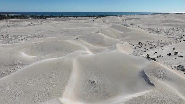 Aerial view of the undulating sand dunes contrasting against the distant blue ocean and sky along Beacon Road, Lancelin, Western Australia, Australia.