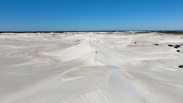 Aerial view of pristine white sand dunes contrasting with the clear blue sky, with people enjoying recreational activities, Lancelin, Western Australia, Australia.