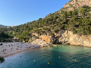 Sandy beach cove with turquoise water and rocky cliffs, people relaxing under the sun