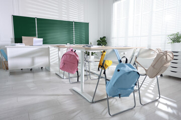 Green chalkboard, desks and chairs with backpacks in classroom