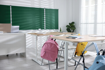 Green chalkboard, desks and chairs with backpacks in classroom