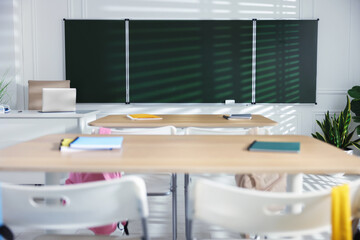 Green chalkboard, desks and chairs with backpacks in classroom